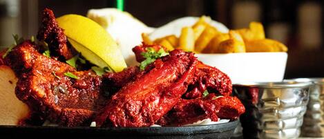 A plate of red, glazed chicken wings with lemon wedges and a side of golden fries.