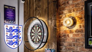 A dartboard mounted on a wooden wall with a dartboard sign below it. - The Littleover Lodge Hotel (Derby)