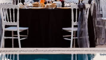 An outdoor dining area with a poolside view, featuring a table set with dinnerware and a chandelier.