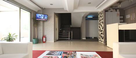 A modern lobby with a flat-screen TV, a staircase, and a reception desk.