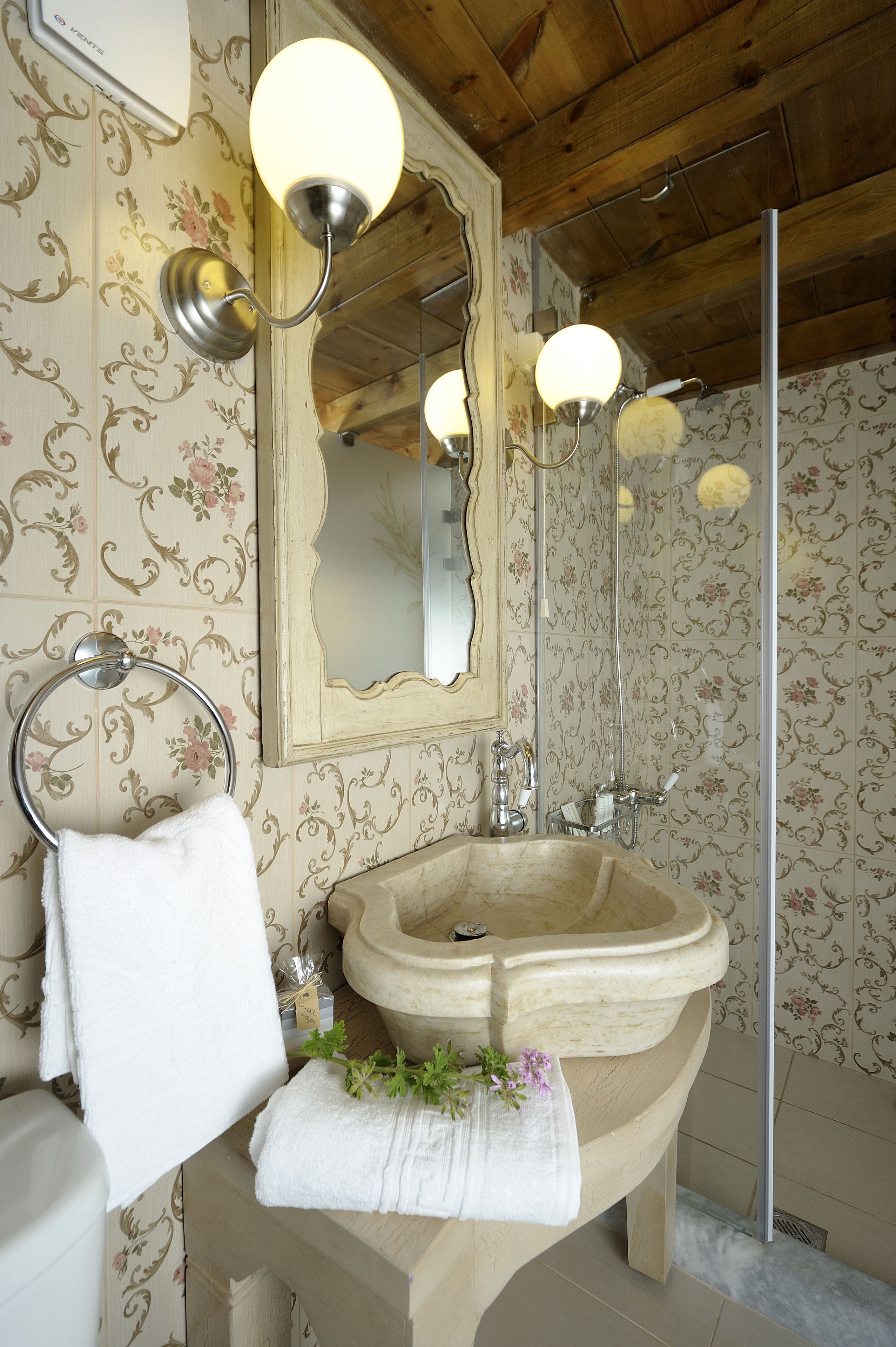 Un baño con un lavamanos de piedra, un espejo y papel tapiz con motivos florales.