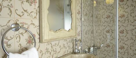 Un bagno con lavandino in pietra, uno specchio e carta da parati con motivi floreali.