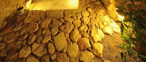 An underground stone room with a wooden bench, a stone bench, and a small window.