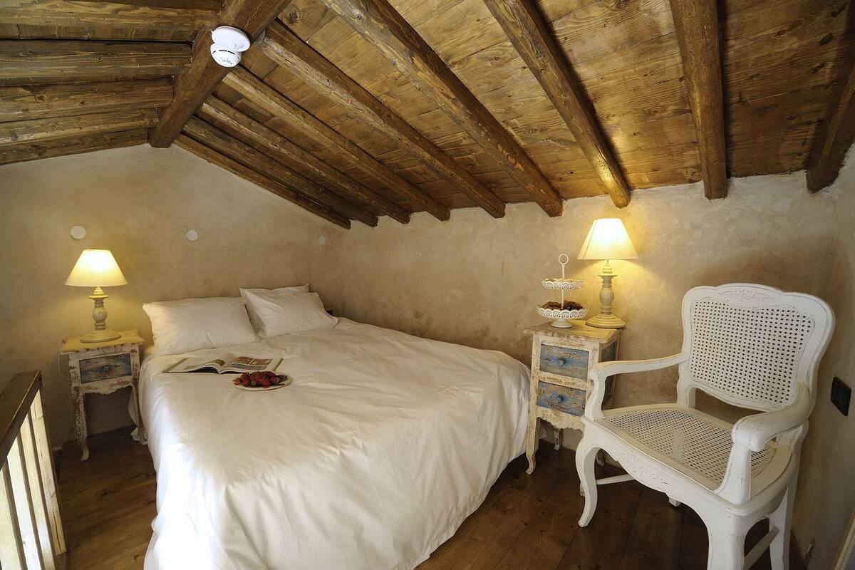 A bedroom with a wooden ceiling, a bed, a chair, and two bedside tables with lamps.