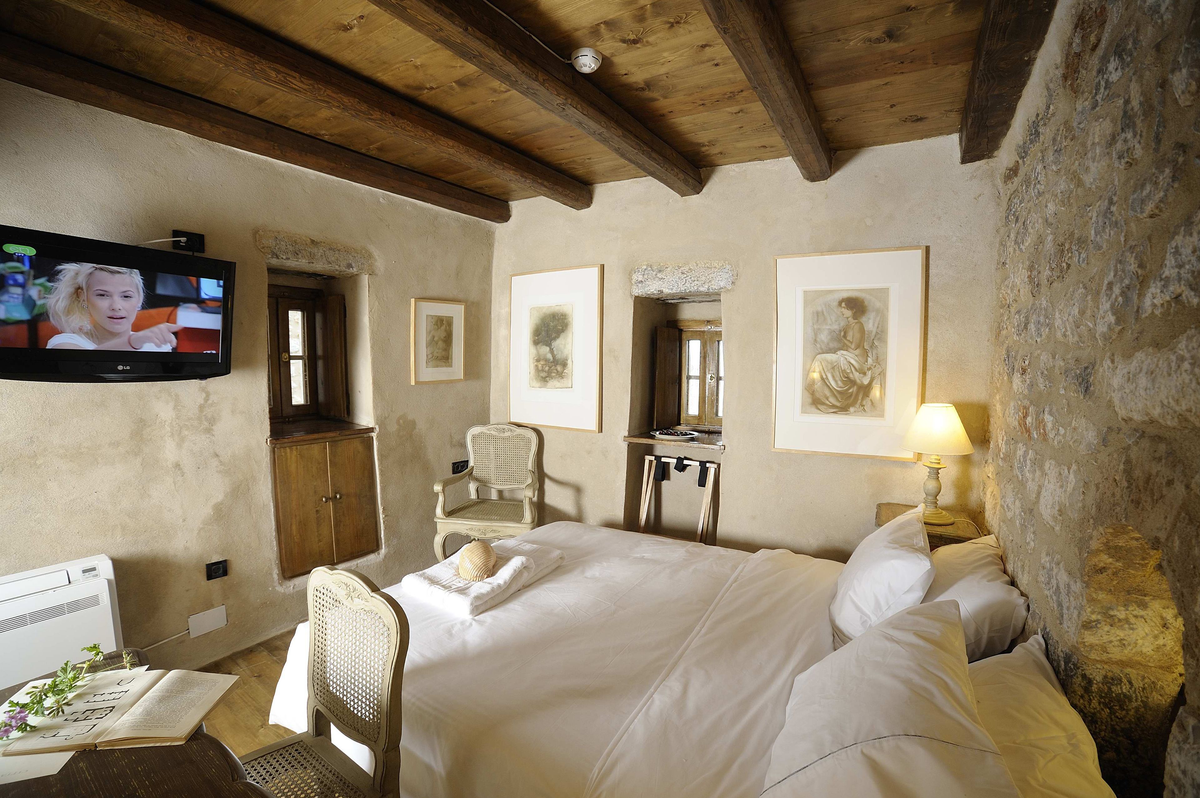 Un dormitori amb sostre de fusta, un llit amb roba blanca, televisió penjada a la paret i obra d'art emmarcada.
