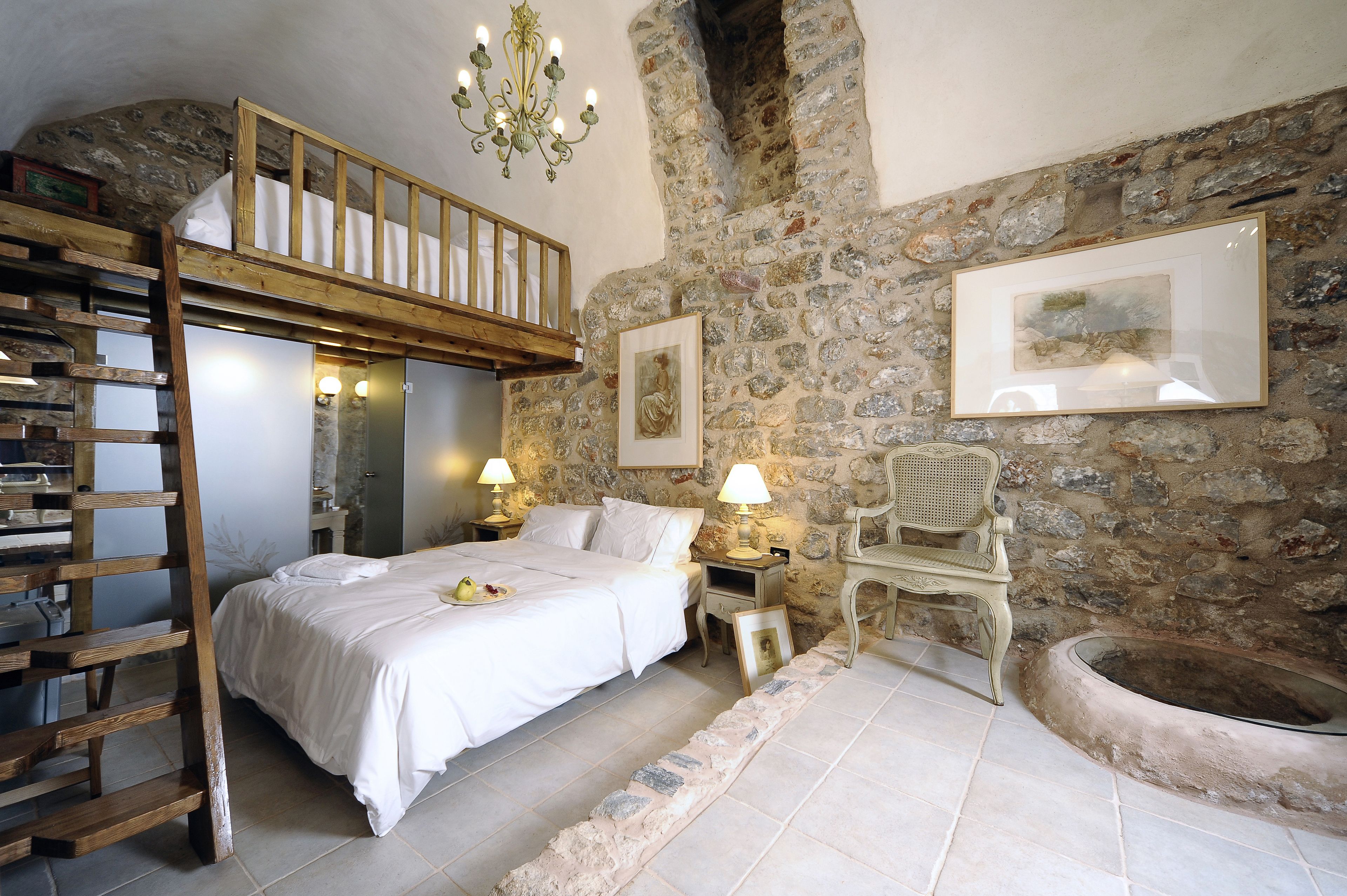 A bedroom with a bunk bed, stone walls, a fireplace, and a wooden ladder.