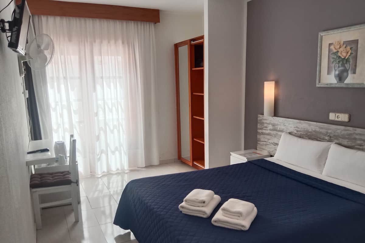 Una habitación de hotel con cama, escritorio, silla, armario y un cuadro en la pared.