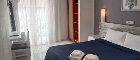 A hotel room with a bed, a desk, a chair, a wardrobe, and a painting on the wall.