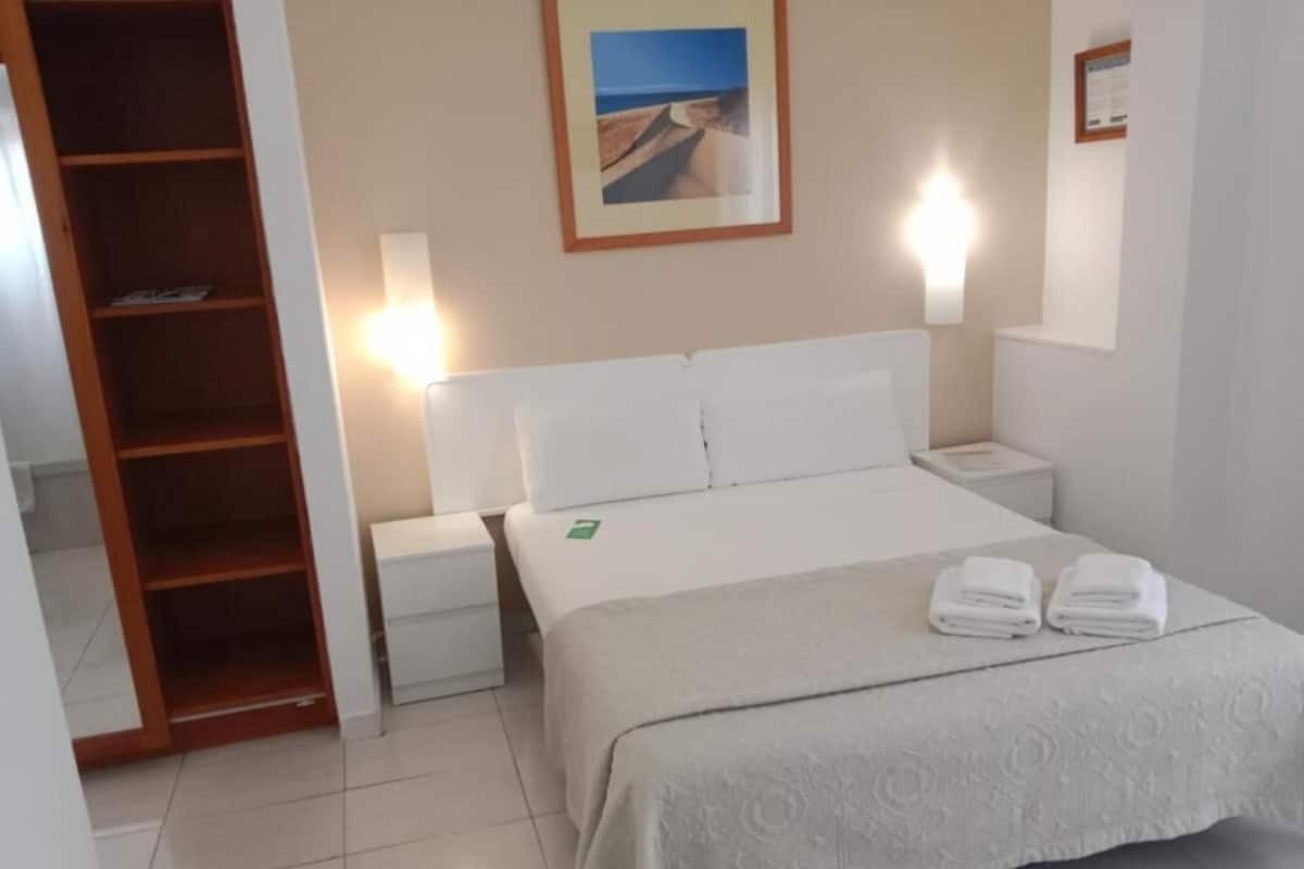 Una habitación de hotel con una cama, mesitas de noche, un armario de madera y un cuadro en la pared.