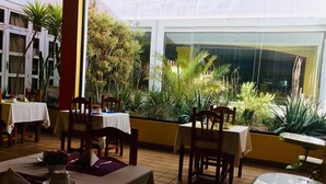 Un restaurante con mesas y sillas, rodeado de plantas y vistas a edificios.