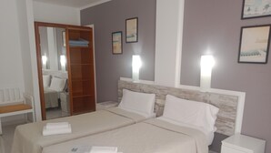 Habitación de hotel con dos camas, un armario de madera, una mesita de noche, una silla y cuadros enmarcados en la pared.
