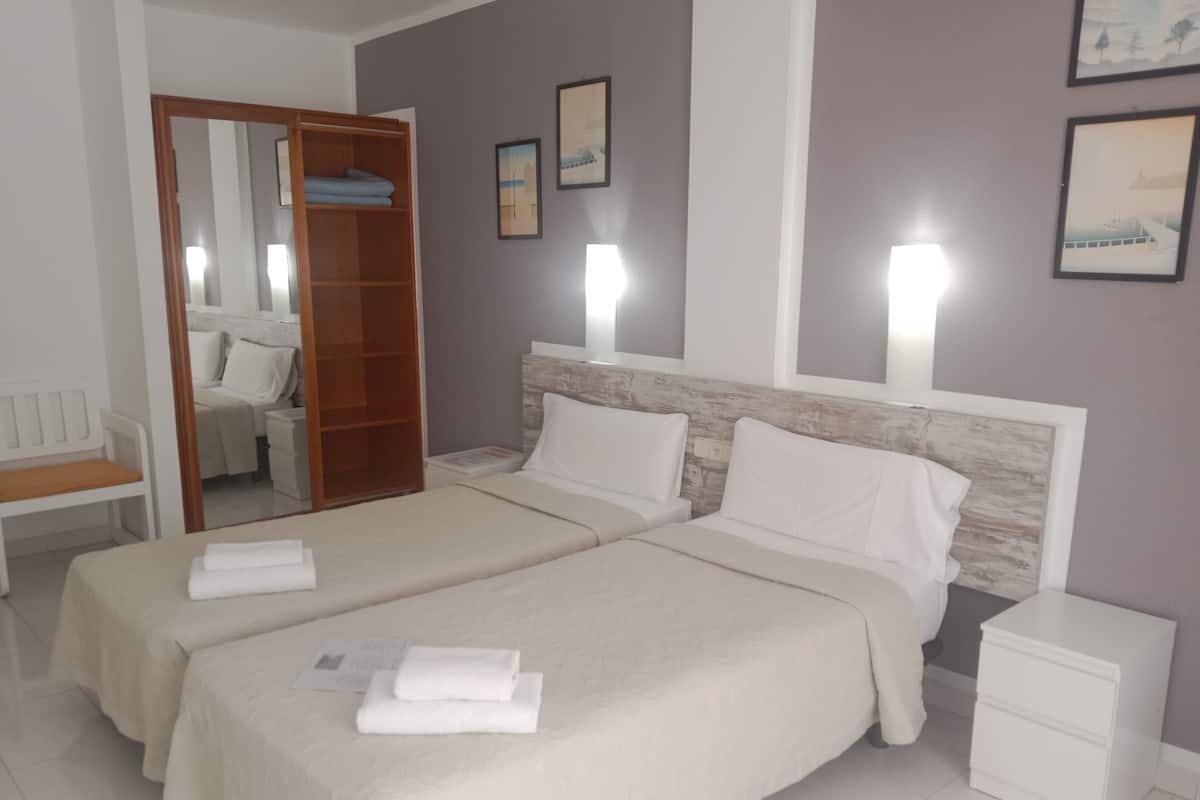 Habitación de hotel con dos camas, un armario de madera, una mesita de noche, una silla y cuadros enmarcados en la pared.