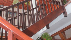 Una escalera de madera de varios niveles con barandillas, rodeada de macetas colgantes.