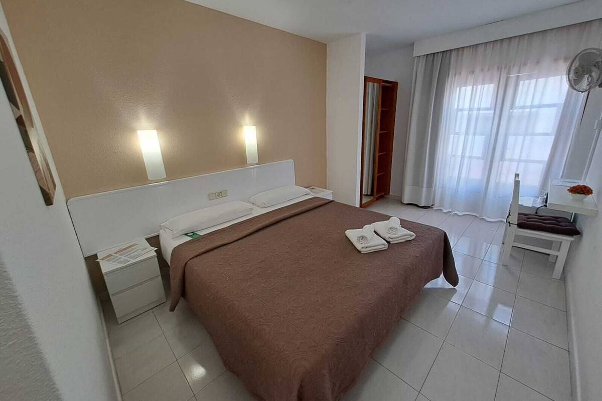 Habitación de hotel con una cama grande, una mesita de noche, un armario y una ventana con cortinas.
