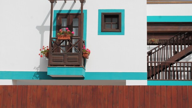 Un edificio con un balcón de madera, una ventana de marco marrón y un ventanal pequeño de marco marrón.