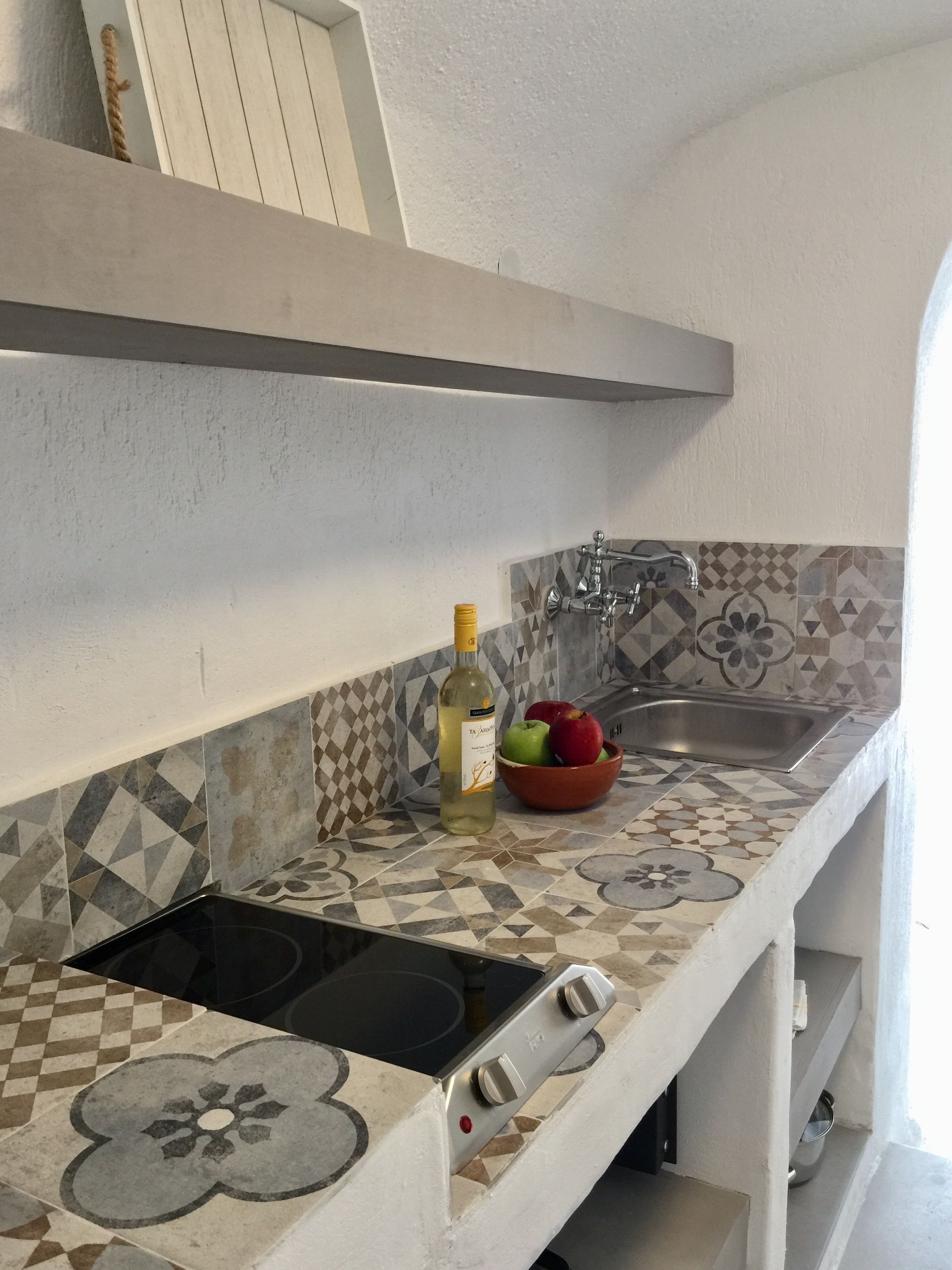 A kitchen with a tiled backsplash, a stainless steel sink, a bottle of olive oil, and a bowl of fruit.