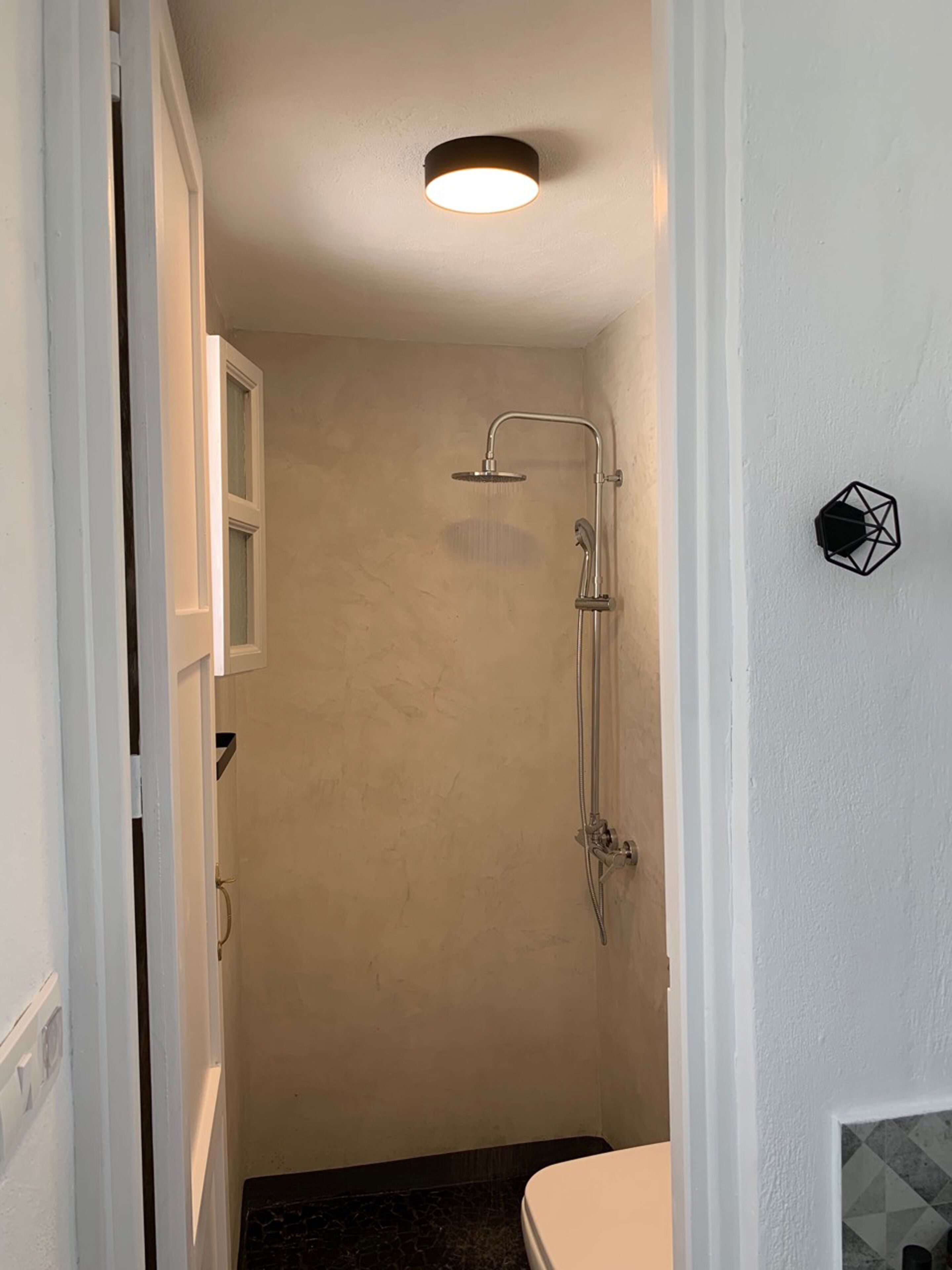 A small, narrow bathroom with a shower, a toilet, and a door leading to another room.