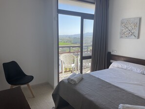 Une chambre d’hôtel avec un lit, une chaise et un balcon donnant sur la campagne.