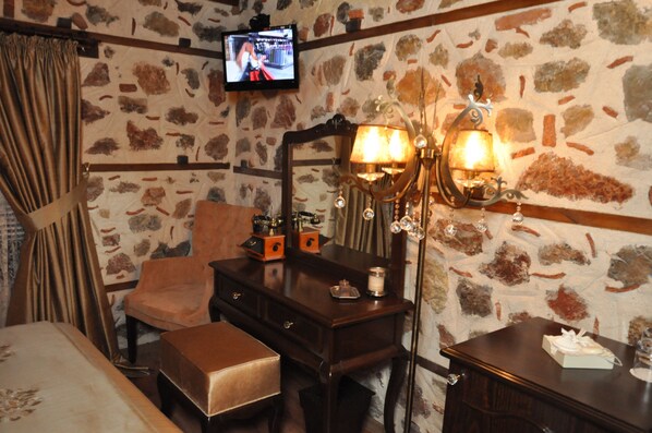 Una habitación con pared de piedra, tocador de madera, una silla, una cama y un televisor montado en la pared.