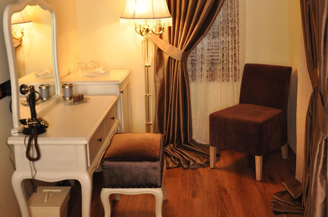 A room with a white dresser, a mirror, a lamp, a brown chair, and a curtain.