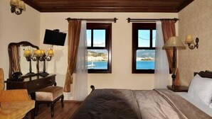 Un dormitorio con una cama, un escritorio con lámpara, dos ventanas con cortinas y un televisor en la pared.