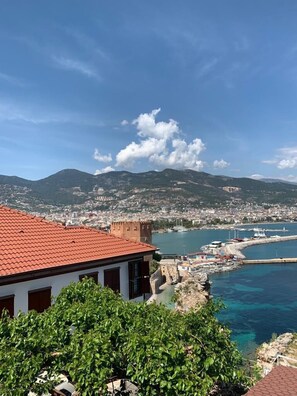 A coastal cityscape with a prominent red-roofed building in the foreground, a marina with boats, and a mountainous backdrop under a clear sky. - Harmony Boutique Hotel (Alanya)