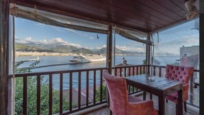 A covered outdoor seating area with a table and chairs, overlooking a body of water with boats and a distant shoreline. - Harmony Boutique Hotel (Alanya)