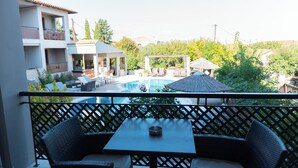 A balcony with wicker furniture, a pool, and a view of surrounding buildings. - Stamos Hotel (Kassandra)