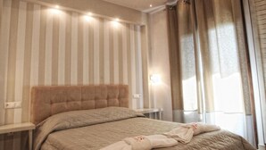 A hotel room with a large bed, a bedside table, a nightstand, and a window with curtains. - Stamos Hotel (Kassandra)