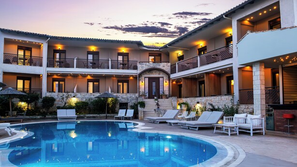 A pool area with lounge chairs and a stone building with multiple balconies. - Stamos Hotel (Kassandra)