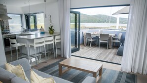 A modern living area with a kitchen, dining space, and a balcony with a view of the water. - Turbine Hotel and Spa (Knysna)