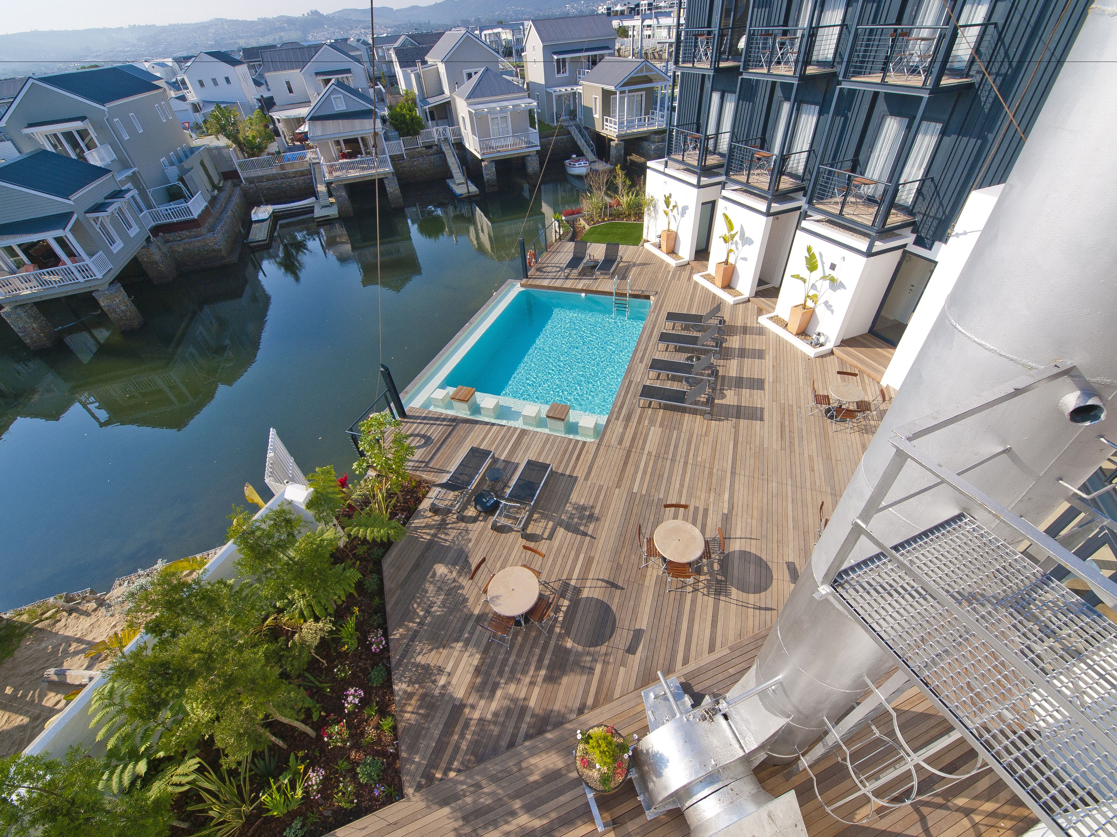 A rooftop pool area with lounge chairs and a small pool, surrounded by residential buildings and a body of water.