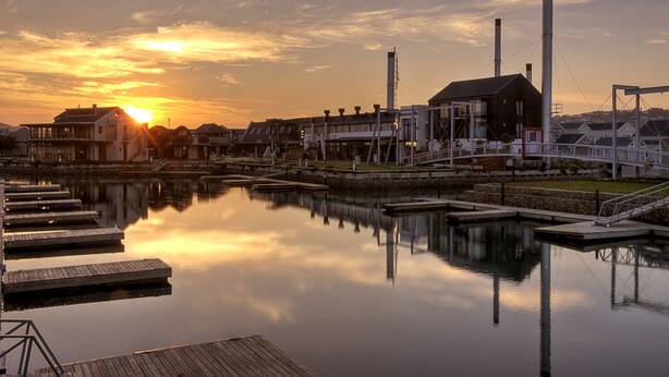 A waterfront property with docked boats, a marina, and industrial buildings with chimneys. - Turbine Hotel and Spa (Knysna)