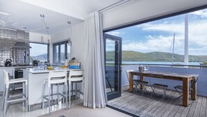 A modern kitchen with a bar area, large windows, and a view of a body of water and hills. - Turbine Hotel and Spa (Knysna)