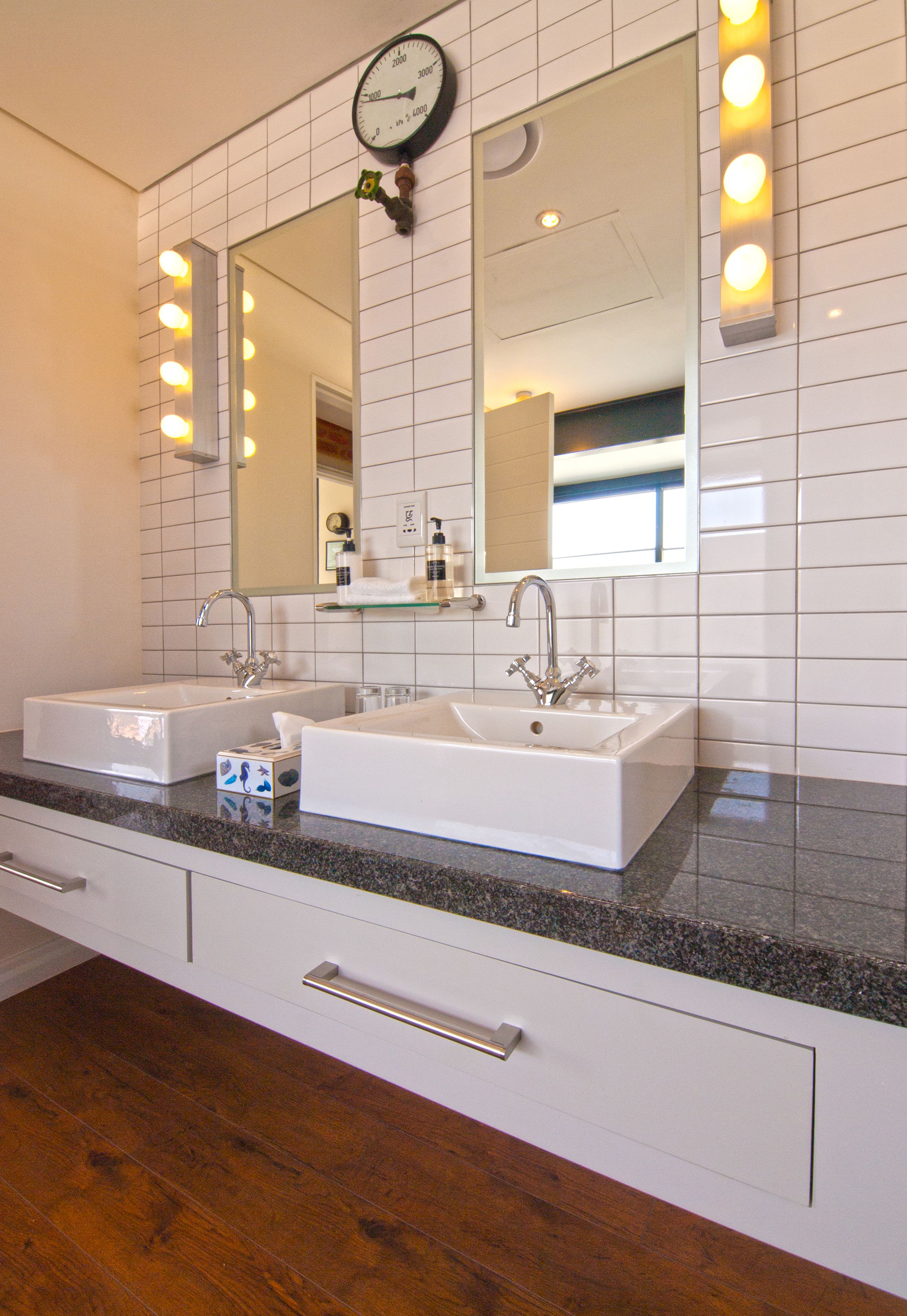 A bathroom with two sinks, a large mirror, and a clock above the mirror.