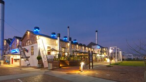 A waterfront hotel with a brick facade, outdoor seating, and a visible staircase leading to the entrance. - Turbine Hotel and Spa (Knysna)