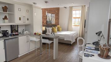 A compact hotel room with a kitchenette, a bed with a headboard, a dining area, and a bathroom.