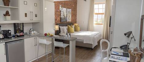 Habitación de hotel pequeña con kitchenette, una cama con cabecera, zona de comedor y baño.