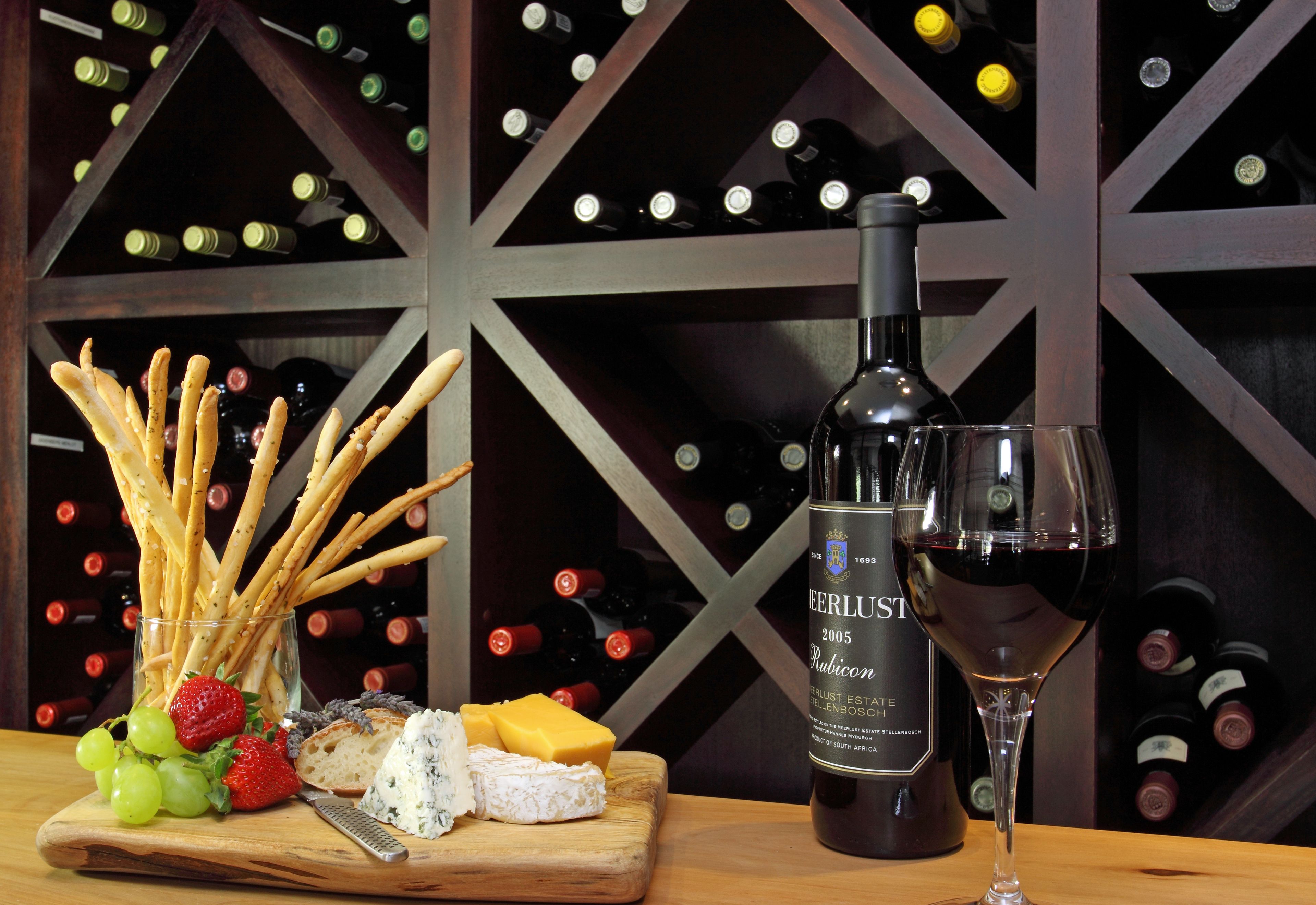 A wooden board with cheese, grapes, and crackers, a bottle of wine, and a wine glass.