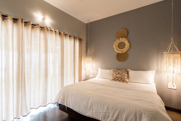A bedroom with a large bed, curtains, wall decor, and hanging lights.