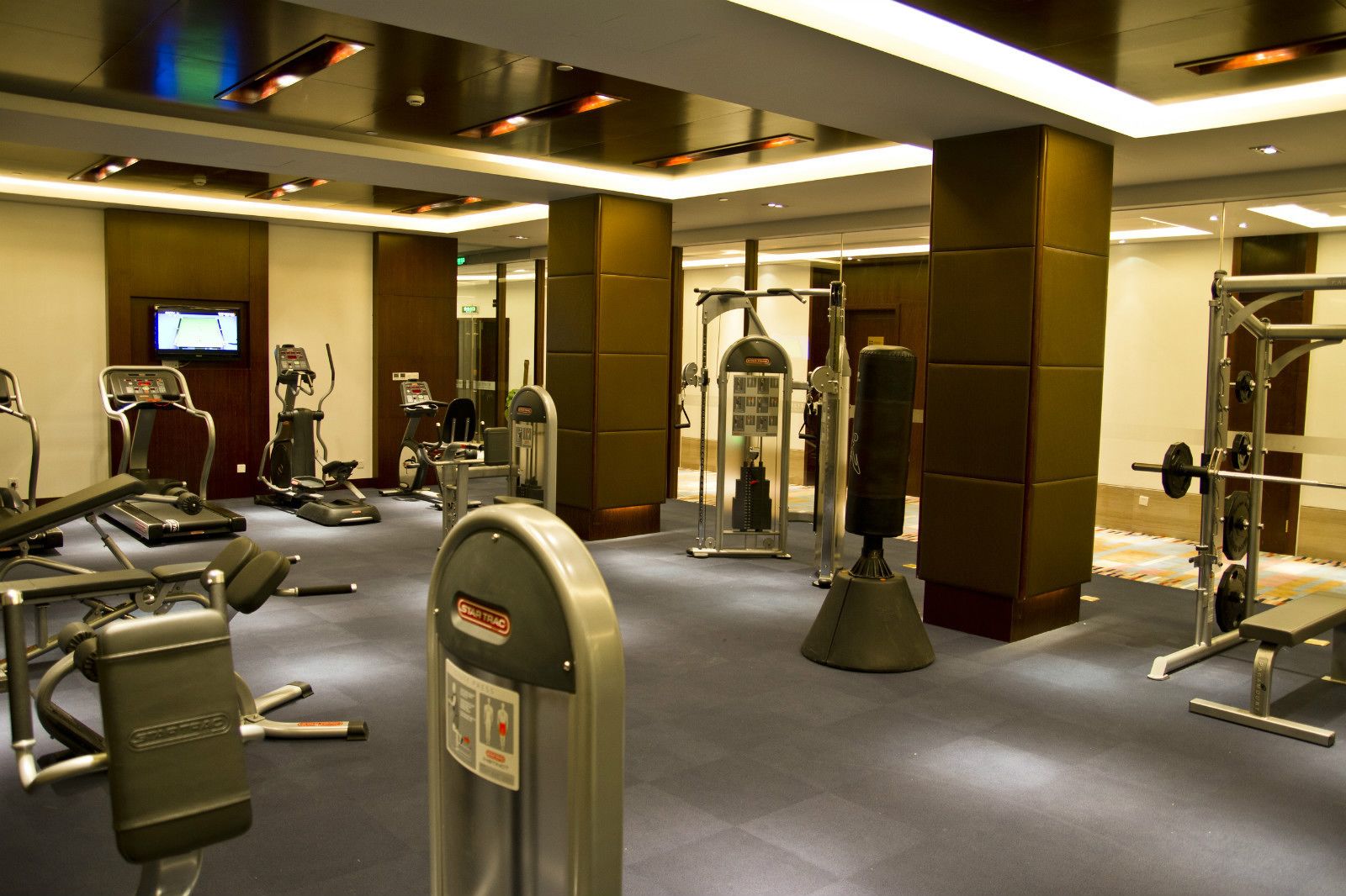 A well-equipped gym with various cardio machines, weightlifting equipment, and a television screen displaying a sports channel.