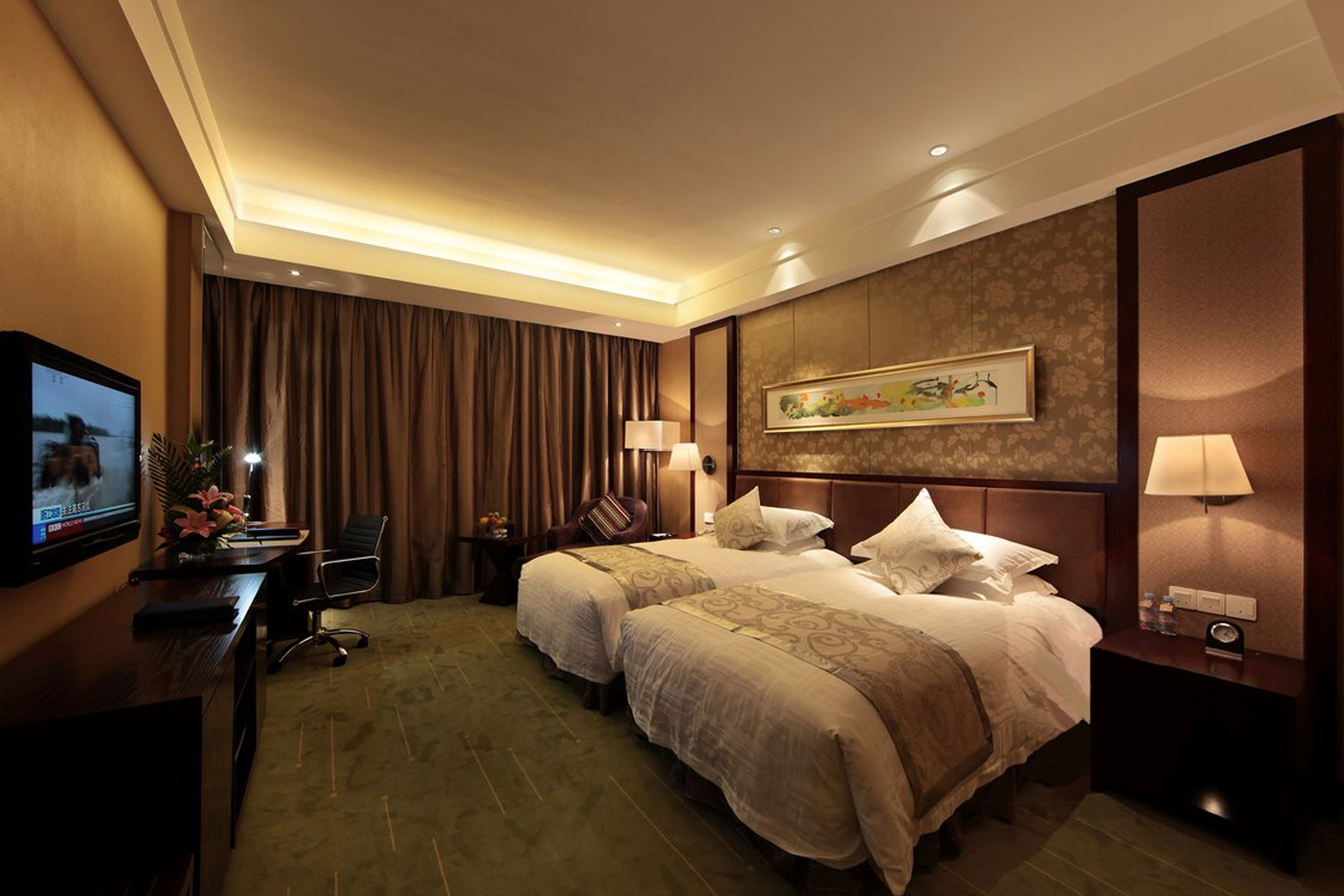 Ein Hotelzimmer mit zwei Betten, einem Schreibtisch mit Fernseher, einem Sessel, einem Nachttisch und einem Bild an der Wand.