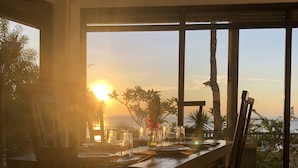 A dining area with a large table set for six, positioned near a large window with a view of the sunset and palm trees. - Argonauta Boracay Boutique Hotel with Apartments and Villas (Boracay Island)