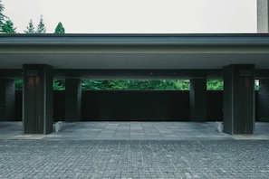 A covered outdoor area with a paved floor, stone pillars, and a view of trees in the background.