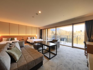 A modern hotel room with a large bed, a sofa, a dining table, and a balcony with a mountain view.
