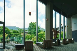 A spacious indoor area with large windows offering a view of greenery and mountains. There are several seating areas with chairs and a table.