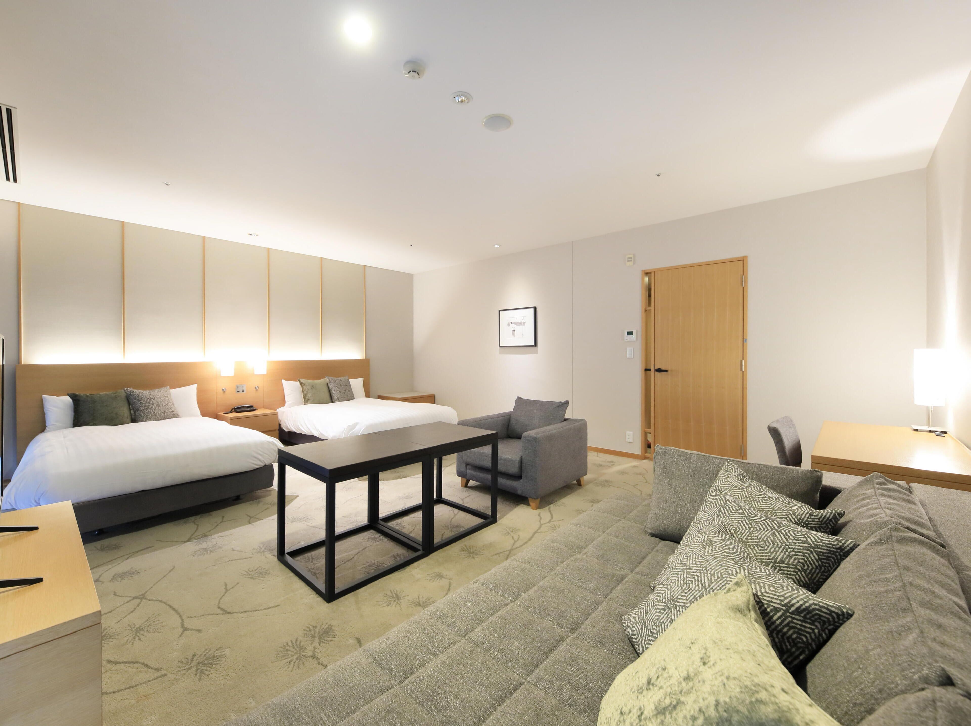 Una habitación de hotel moderna con una cama grande, un sofá, una mesita pequeña y una puerta de madera.