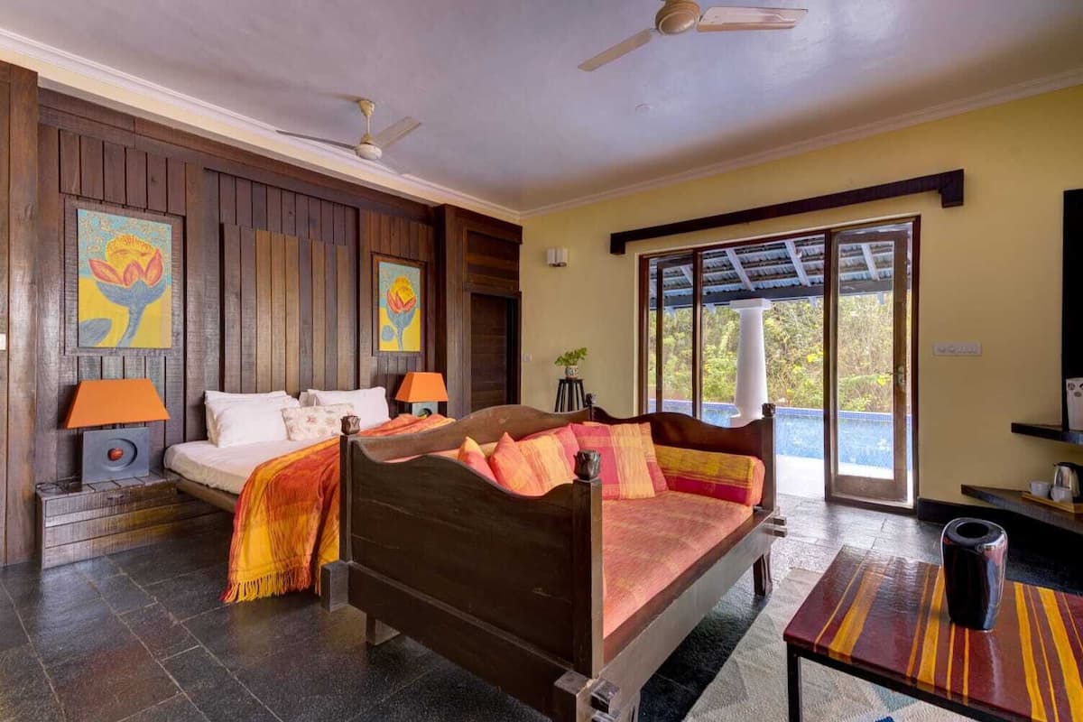 A room with a bed, two bedside tables, a sofa, a ceiling fan, and a large window with a view.