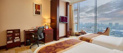A hotel room with two beds, a desk with a chair, a TV, and a large window with a city view.