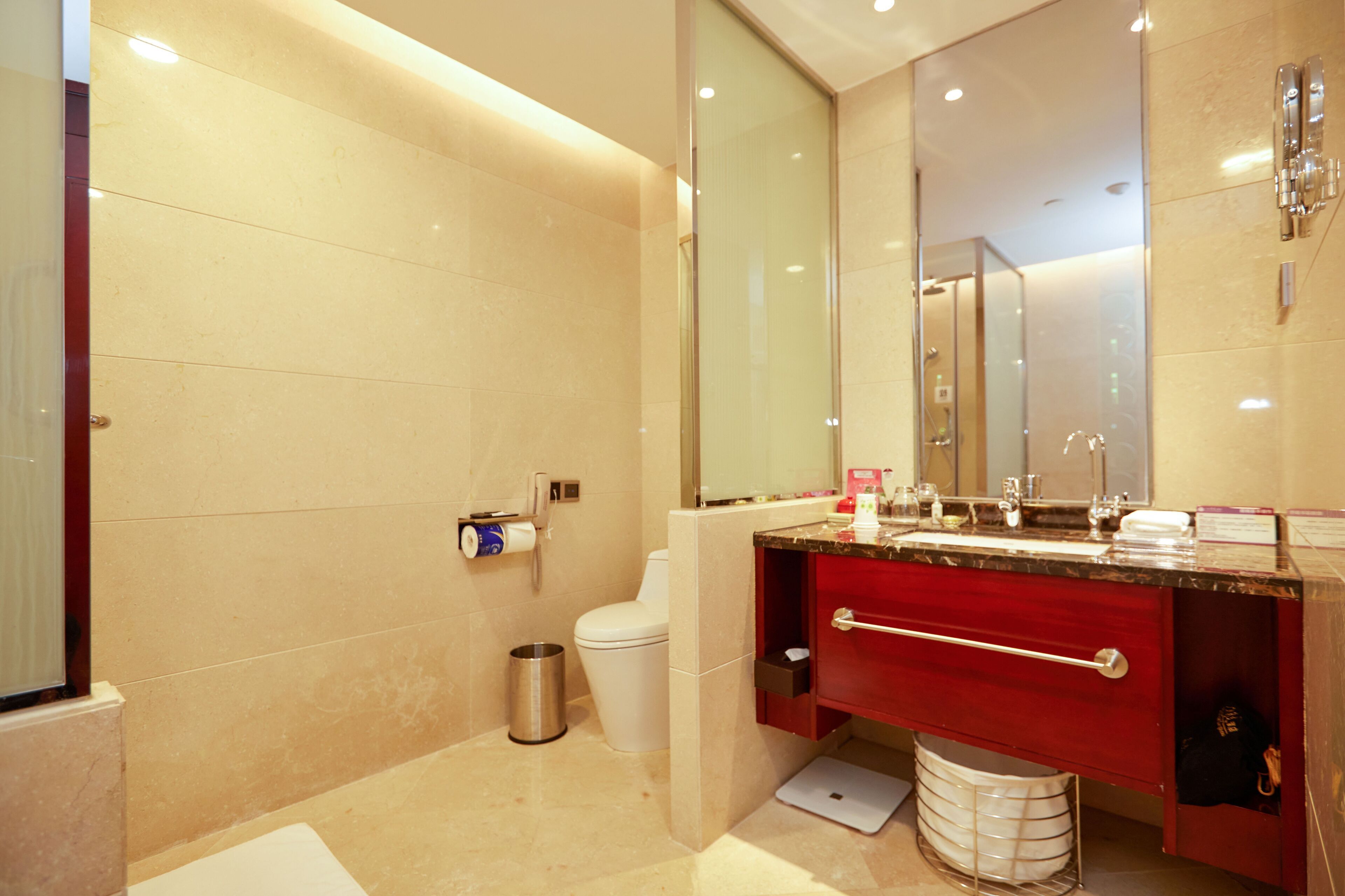A modern bathroom with a large mirror, a red vanity, a white toilet, and a glass shower enclosure.
